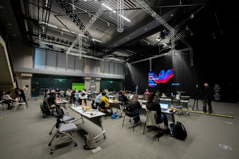 A diverse group attending an educational seminar with screens and seating indoors, highlighting collaboration.